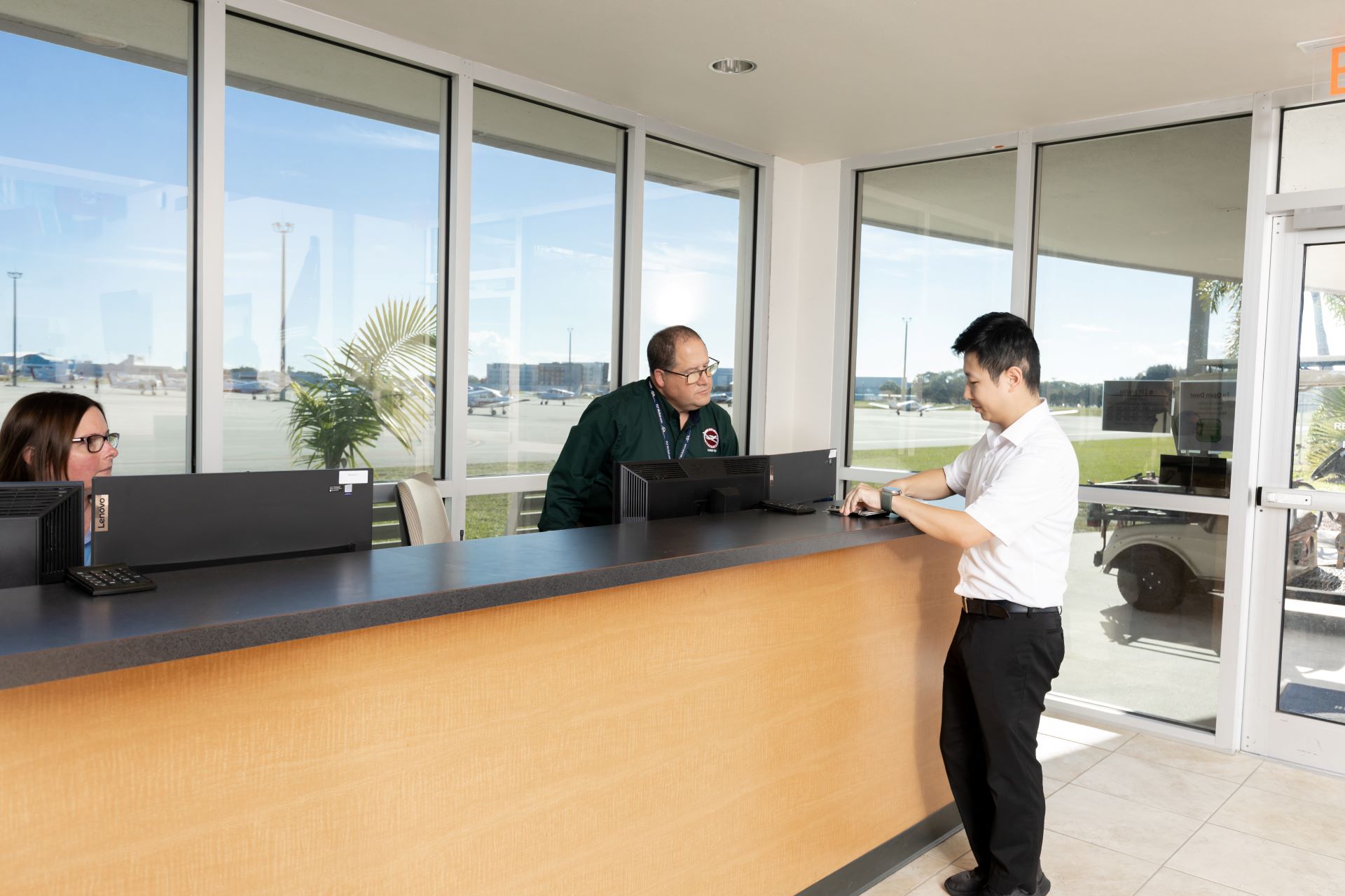 A student presenting something to a university receptionist, while another receptionist listens
